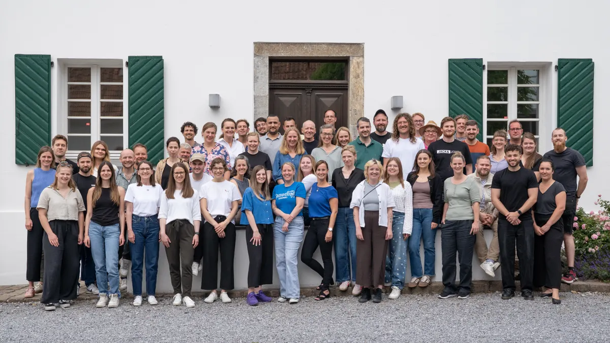 Gruppenfoto aller Mitarbeitenden der matrix Gruppe unter freiem Himmel vor einem weißen Gebäude