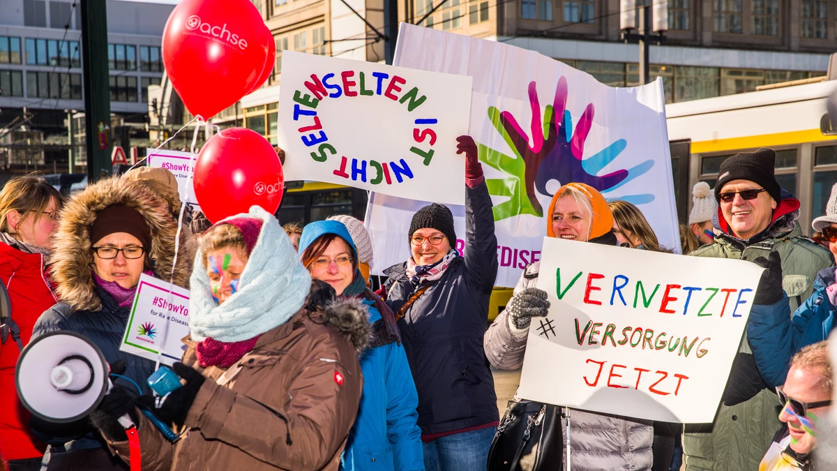 Personengruppen angeschnitten, alle winterlich dick angezogen, mit Ballons, Megafon und selbstgemalten Bannern, auf denen u.a. steht "Selten ist nicht selten" und "Vernetzte Versorgung jetzt"