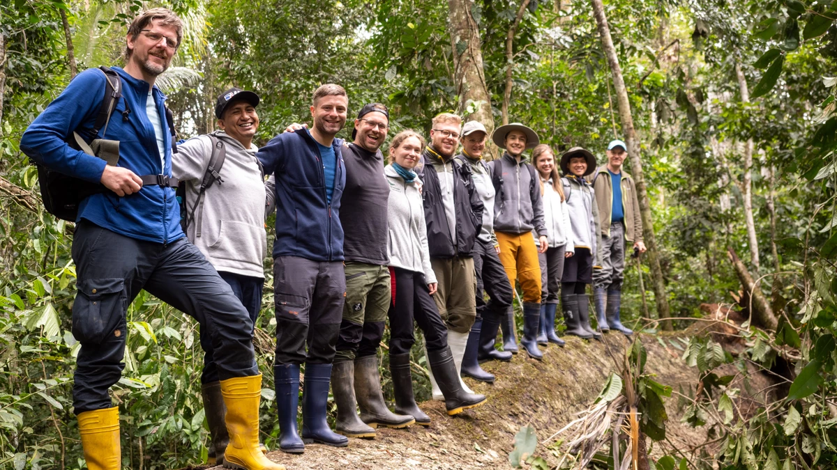 Das Team von Wilderness International steht im peruanischen Regenwald auf einem umgefallenen Baumstamm