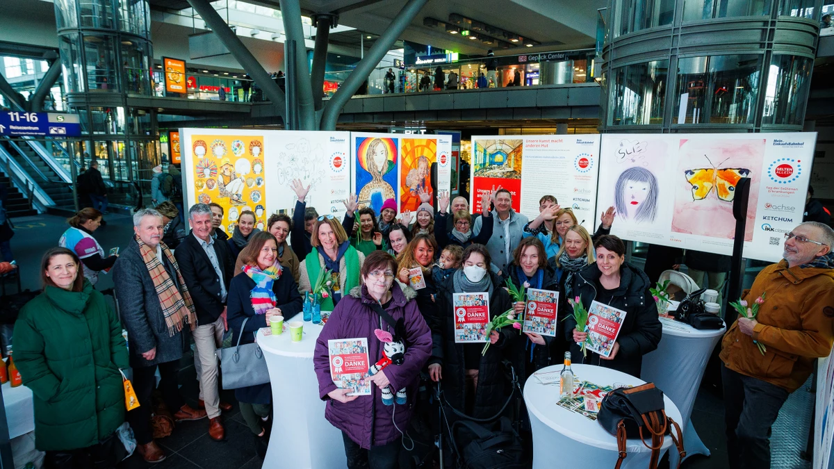 Personengruppe an Stehtischen, im Hintergrund Bilder der Ausstellung Selten allein, die hier eröffnet wurde - zu sehen auch die Halle des Hauptbahnhof Berlin von Innen.