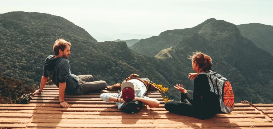 drei Menschen sitzen auf einer Terrasse vor einem Gebirge 