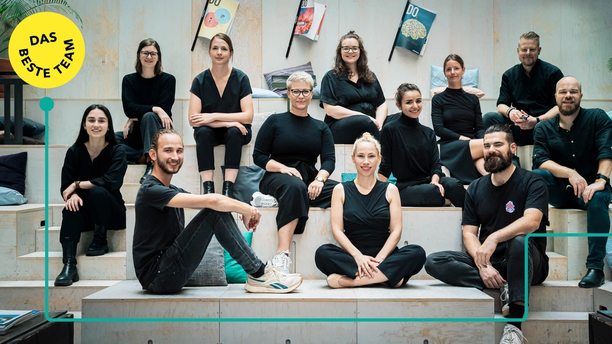 Gruppenfoto vom Team, alle in schwarzer Kleidung auf einer Tribüne sitzend und in die Kamera lächelnd