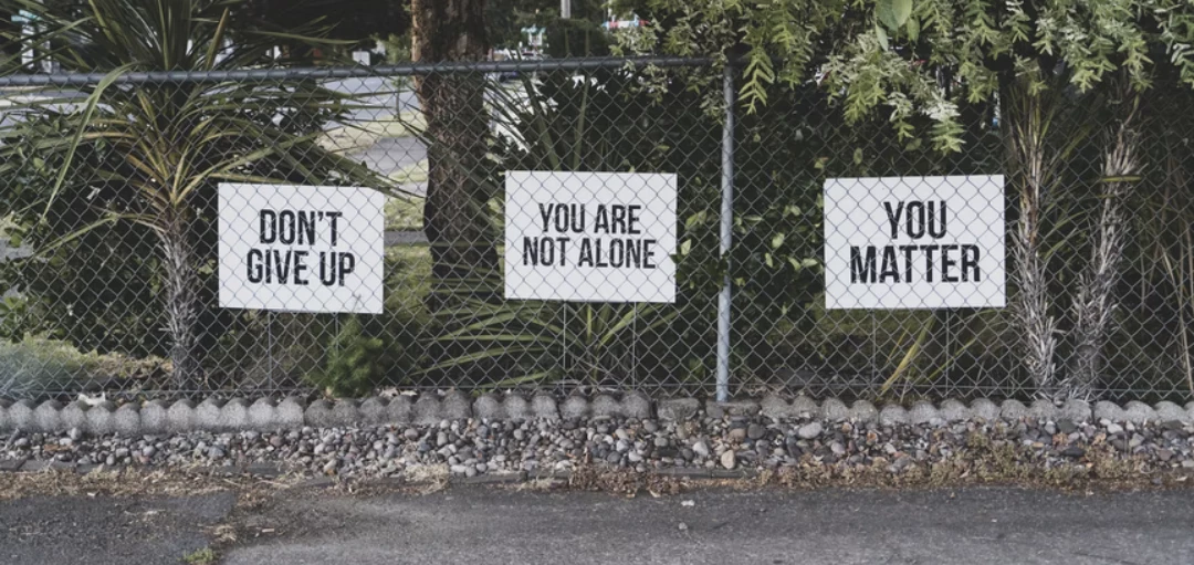 Zaun mit Schildern: Don't give up, You are not alone, You matter – Psychische Krankheiten am Arbeitsplatz 