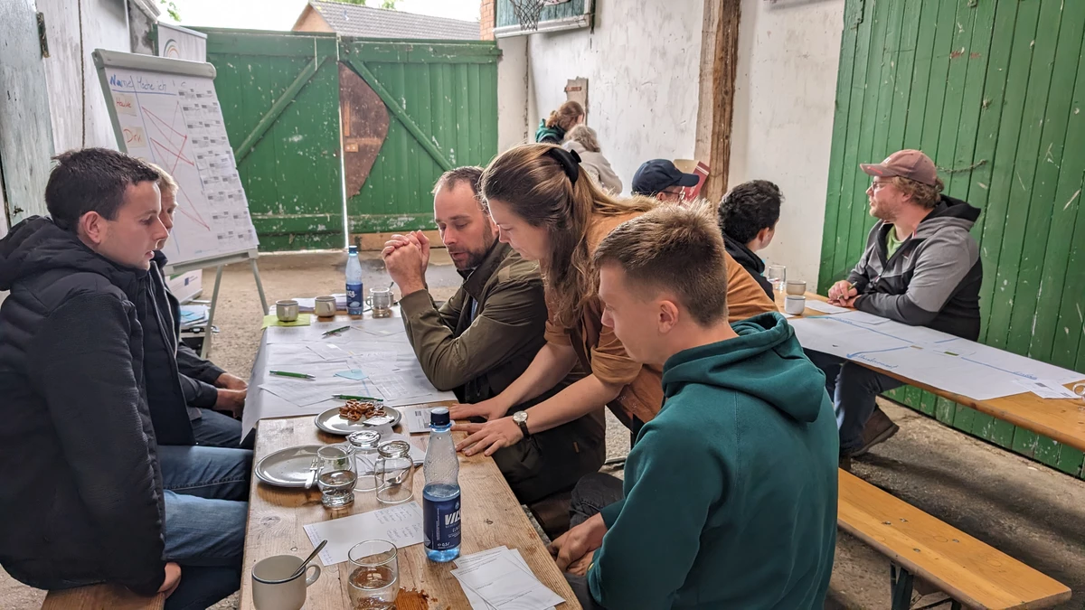 Eine Gruppe von Menschen sitzt im Stall an einem Tisch und tauscht sich aus.