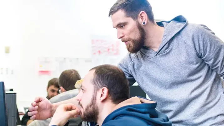 Ein IT-Mitarbeiter hilft einem sehbeeinträchtigten Mann bei der Bedienung eines Laptops