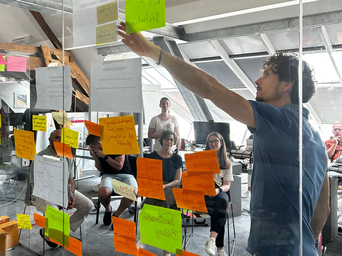 Workshop-Situation durch eine Glasscheibe fotografiert, die gleichzeitig als Pinnwand dient