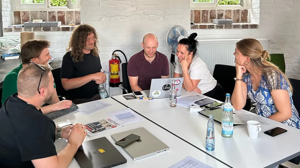 Gruppenarbeit-Situation mit sechs Personen an einem Tisch die auf einen Laptop gucken