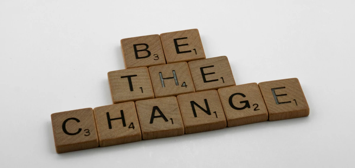 Holzbuchstaben liegen auf weißem Hintergrund und bilden die Worte "Be the change". Das Bild symbolisiert Selbstwirksamkeit – die Überzeugung, durch das eigene Handeln Veränderungen bewirken zu können. 