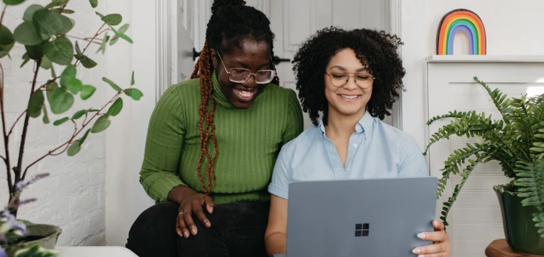 Zwei Menschen die auf einen Laptop schauen, Pflanzen und Regenbogen im Hintergrund 