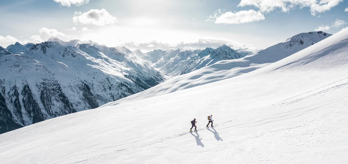 Zwei Menschen in Winterkleidung wandern durch Schnee bergauf. 