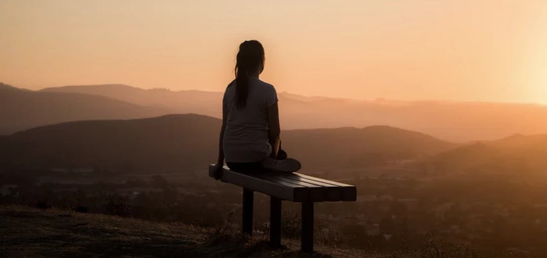 Person sitzt im Sonnenaufgang auf einer Bank und beobachtet die Aussicht 