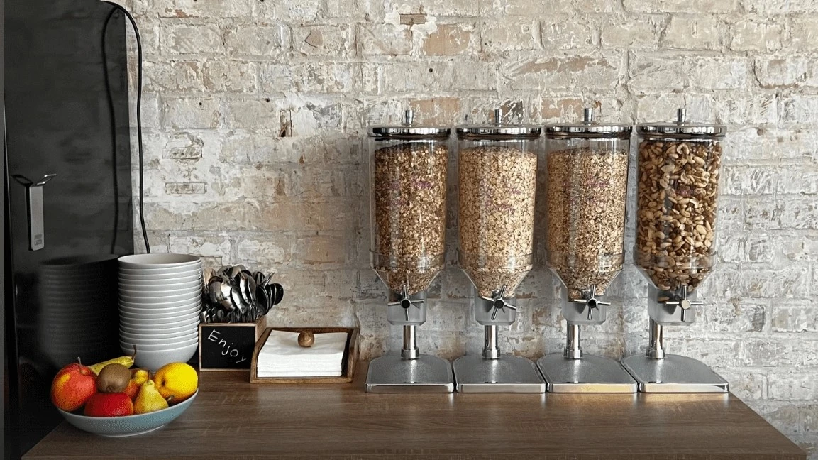 A picture of the Patronus breakfast bar. Different types of granola and nuts, boals and spoons are in the picture, and on the table is a plate with fresh fruits.