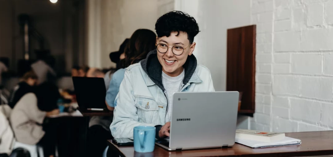 Person sitzt in einem Café am Laptop und lacht 