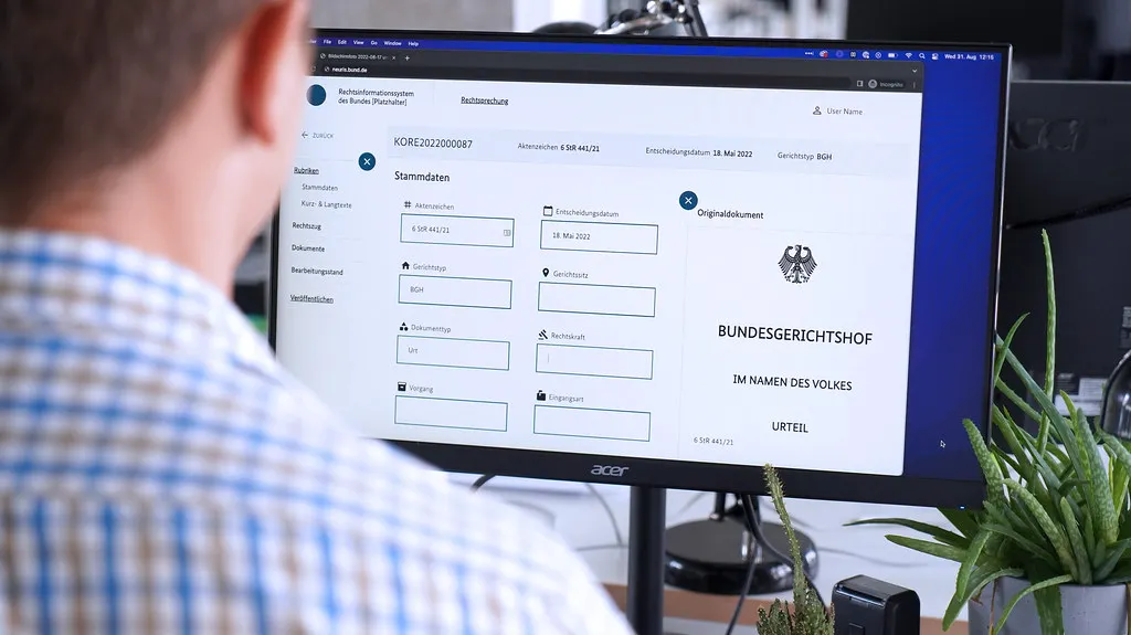 Ein Mann im Hemd sitzt vor einem Computer. Auf dem Bildschirm ist die Benutzeroberfläche der NeuRis Plattform zu erkennen.