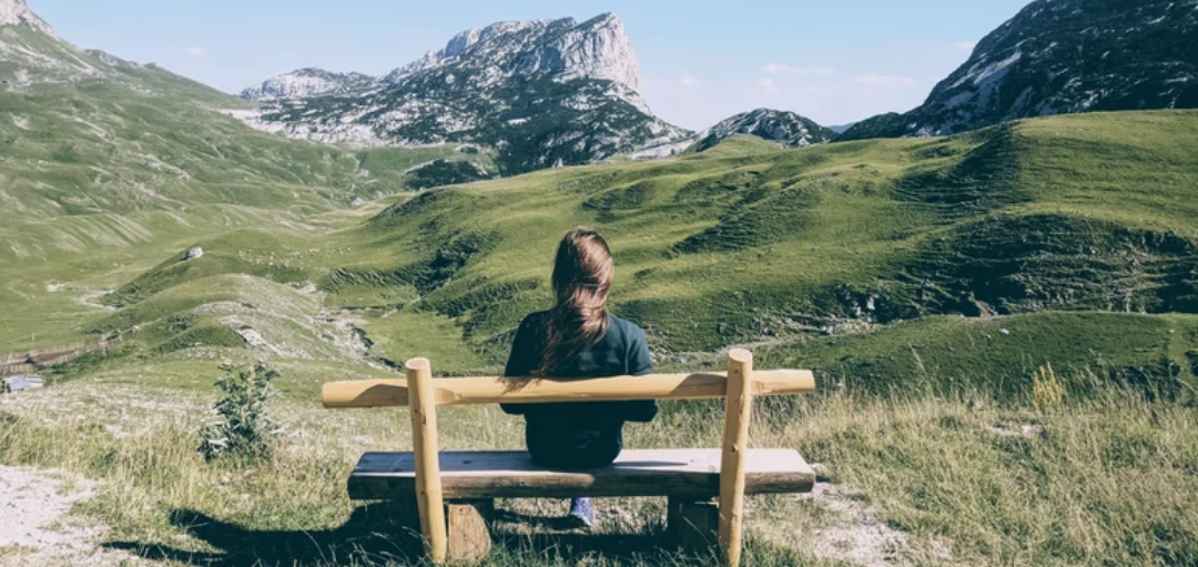 Frau sitzt auf einer Holzbank in den Bergen - Sicht von hinten 