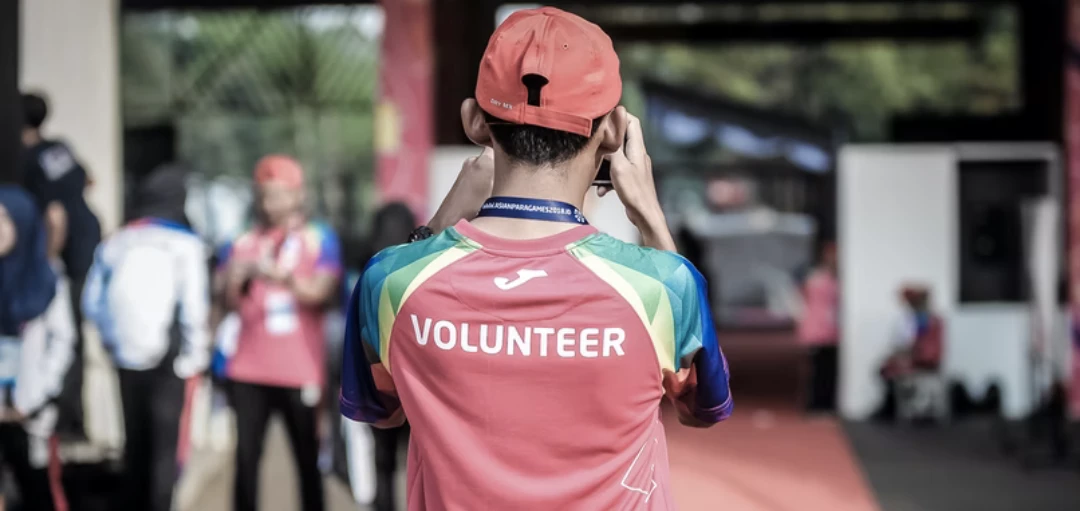 Person von Hinten mit rotem T-Shirt mit "Volunteer" Aufschrift und roter Kappe 