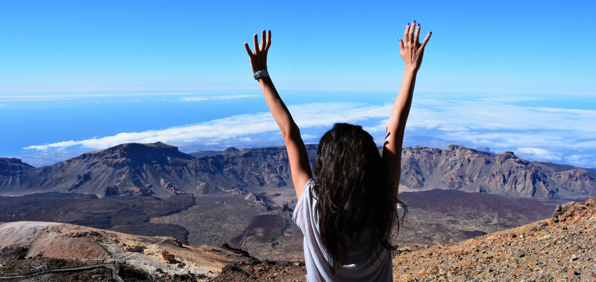 Eine Frau steht mit ausgestreckten Armen vor einem Bergpanorama auf Teneriffa 