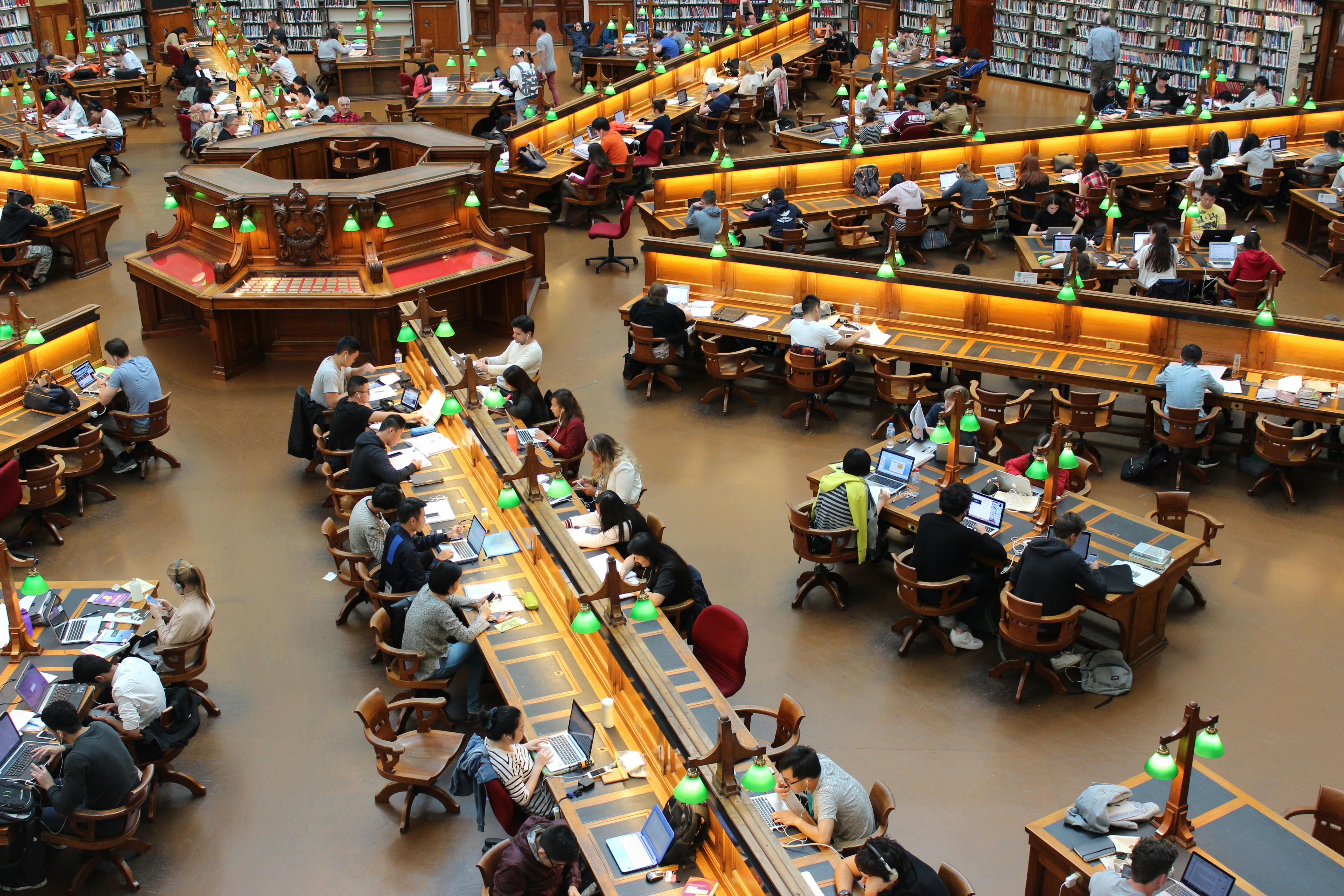 In einer Bibliothek stehen die Schreibtische Sternförmig zum Zentrum orientert. An ihnen arbeiten zahlreiche Student*innen. 