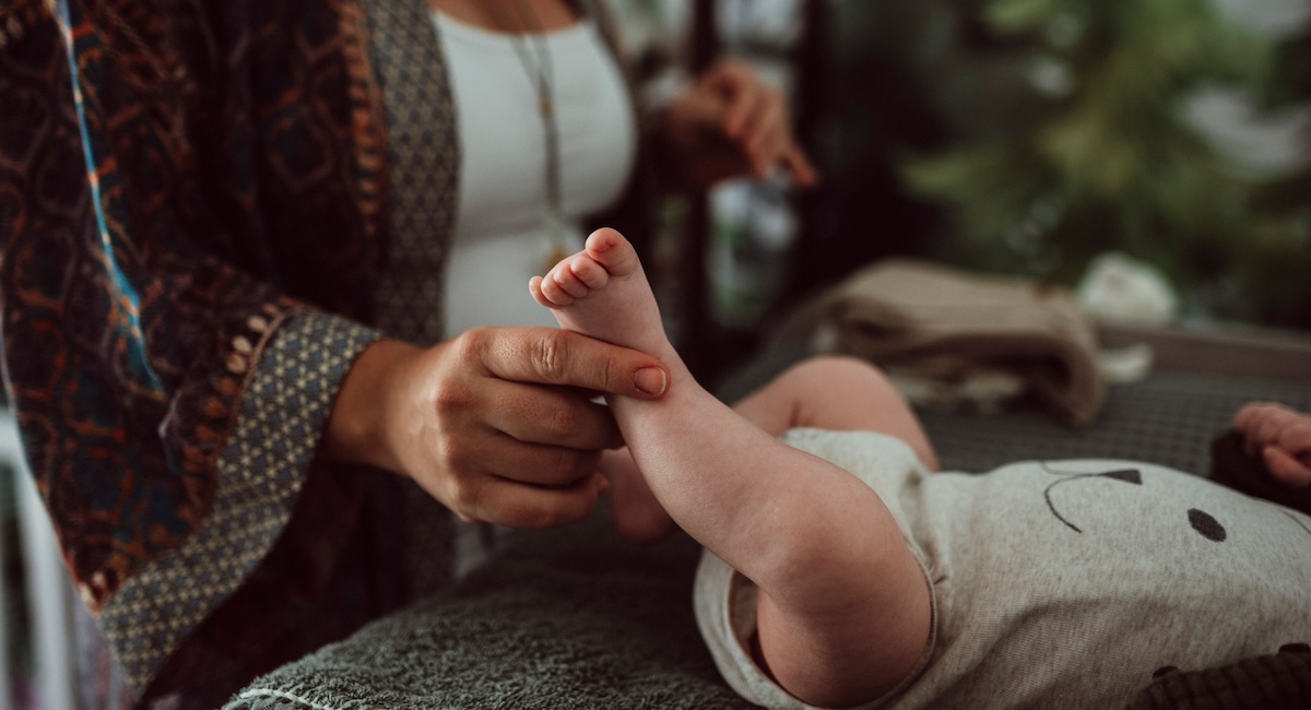 Das Bild zeigt die Hand einer Mutter, die mit den Beinen eines Babies spielt 