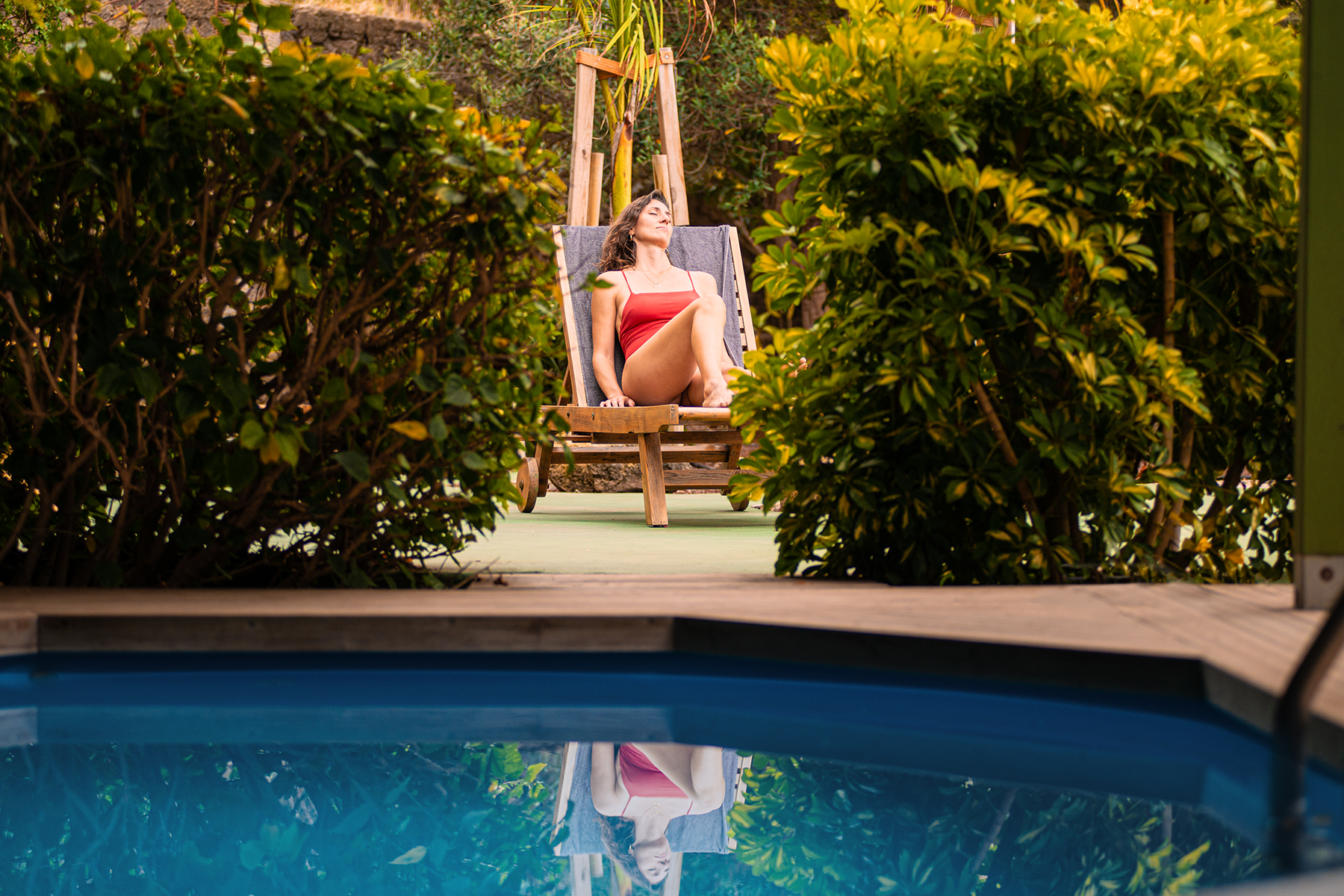 Pool und Gartenliege auf der eine Frau in Badeanzug die Sonne genießt